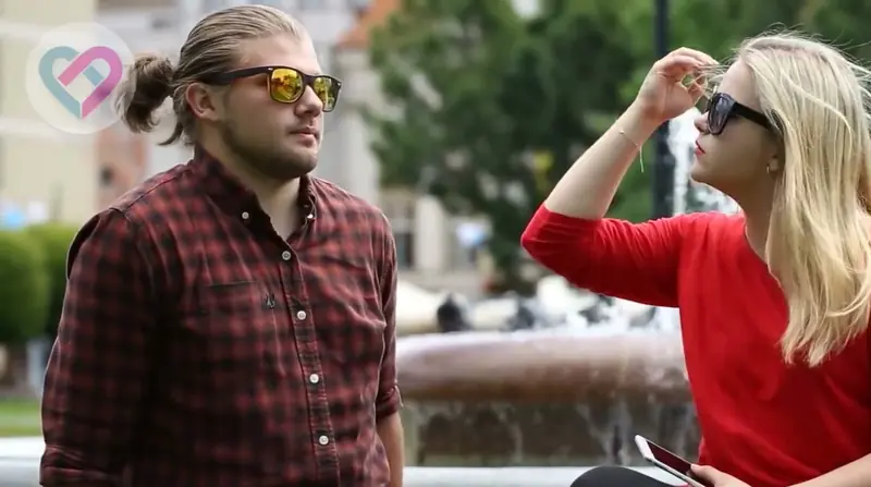 Mujer con el celular en la mano sentada al aire libre junto a un hombre