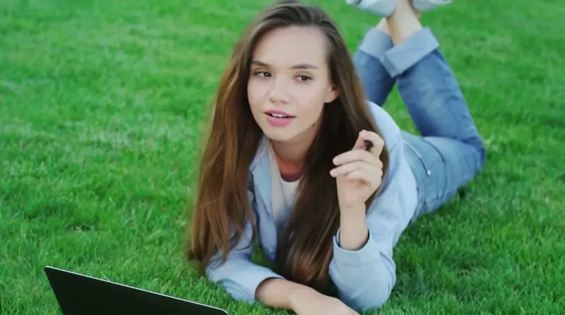 Mujer joven tumbada en el cesped con una laptop y una libreta